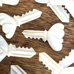 May include: A collection of white, decorative, key-shaped ornaments with a floral design. The ornaments are made of a pearlescent material and have a smooth, polished finish.