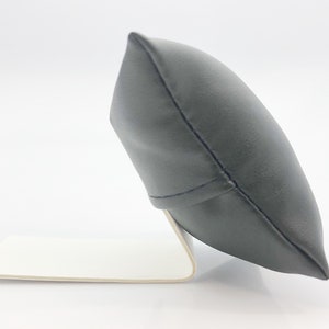 May include: A black leather watch pillow with a white base. The pillow is angled and has a stitched seam down the center.