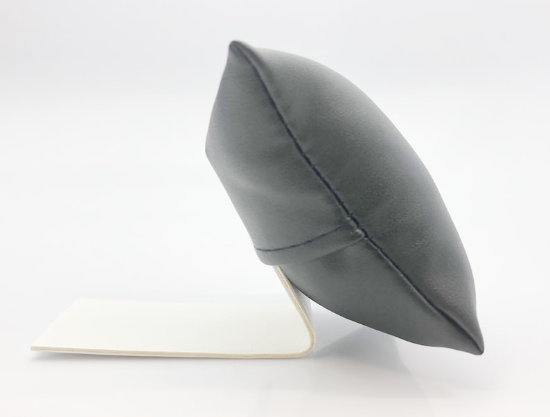 May include: A black leather watch pillow with a white base. The pillow is angled and has a stitched seam down the center.