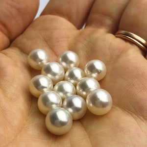 May include: A collection of white pearls in various sizes, displayed in the palm of a hand.