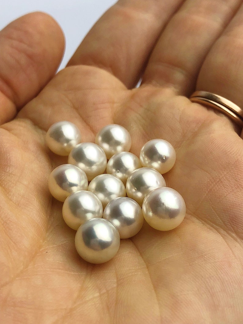 May include: A collection of white pearls in various sizes, displayed in the palm of a hand.
