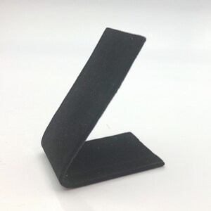 May include: Black velvet ring display stand. The stand is angled and has a rectangular base.
