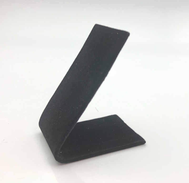 May include: Black velvet ring display stand. The stand is angled and has a rectangular base.