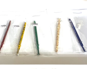 May include: Five colorful wands in clear plastic packaging. The wands are red, yellow, green, cream, and blue. Each wand has a handle and a decorative top. The wands are displayed on a white surface.