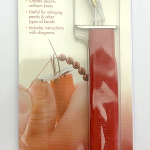 May include: Red plastic bead knotting tool with a gold metal tip. The tool is packaged in a clear plastic bag with a white and red label that reads "the Bead Smith EZKNOT" and "Knotting Tool".