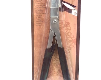 May include: A pair of black handled metal shears with a locking mechanism for safe storage. The shears are packaged on a brown and gold background with the text "VINTAJ META SHEARS" and product features.