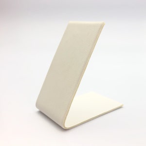 May include: A white, angled display stand made of a textured material. The stand is designed to hold small items, such as jewelry or other accessories.