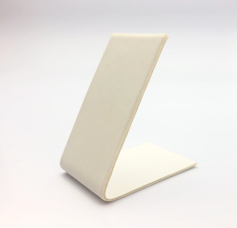 May include: A white, angled display stand made of a textured material. The stand is designed to hold small items, such as jewelry or other accessories.