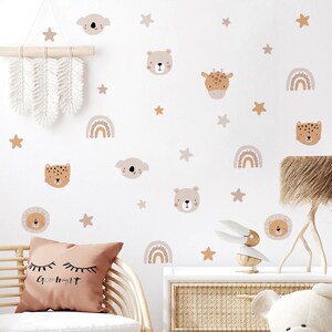May include: A set of wall decals featuring animal faces, rainbows, and stars. The decals are in shades of brown, beige, and pink. The animals include a lion, a bear, a giraffe, a koala, and a leopard. The decals are perfect for a nursery or child's room.