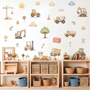 May include: Watercolor wall decals depicting construction vehicles, tools, and a sun. The set includes a crane, excavator, cement mixer, and dump truck. The decals are in shades of yellow, beige, and brown, with green and blue accents. The decals are arranged on a white wall.