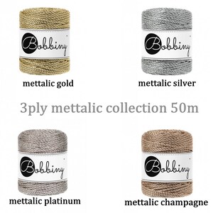 May include: Four spools of 3-ply metallic yarn in gold, silver, platinum, and champagne colors. Each spool is labeled "Bobbiny" and is 50 meters long.