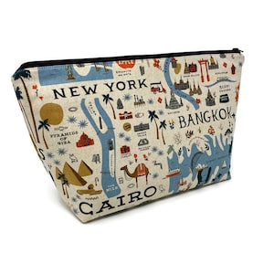 May include: A beige canvas zippered pouch with a colorful map design featuring landmarks from New York, Cairo, and Bangkok. The pouch has a black zipper and a white background.
