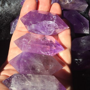 May include: A collection of amethyst crystal points, each with a unique shape and purple hue. The crystals are arranged in a hand, showcasing their natural beauty and clarity.