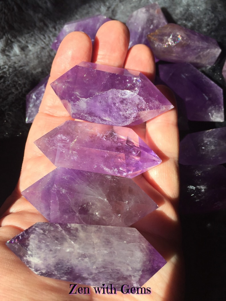 May include: A collection of amethyst crystal points, each with a unique shape and purple hue. The crystals are arranged in a hand, showcasing their natural beauty and clarity.