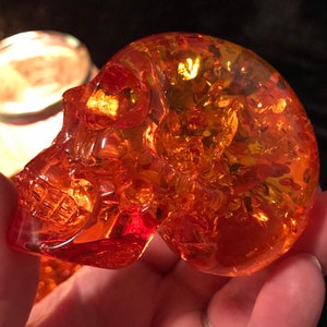 May include: A small, amber-coloured glass skull figurine. The skull is detailed and has a translucent appearance.