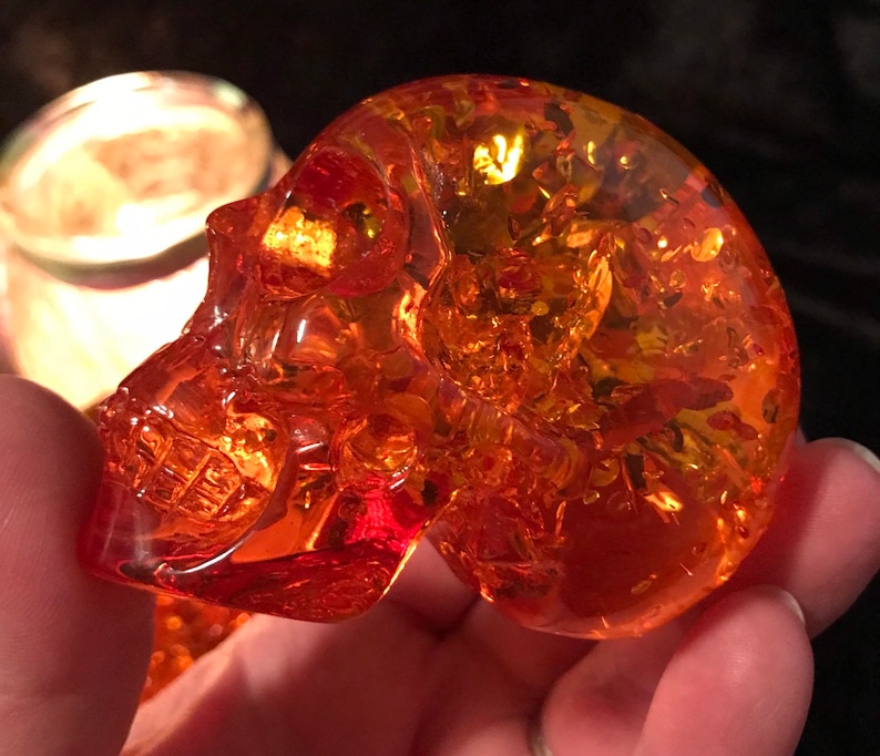 May include: A small, amber-coloured glass skull figurine. The skull is detailed and has a translucent appearance.