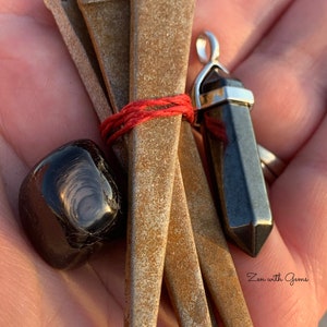 May include: A set of four rusty metal nails tied together with red string, a black obsidian crystal pendant, and a black obsidian tumbled stone. Zen with Gems.