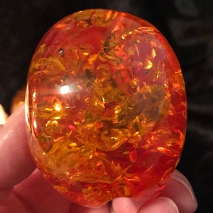 May include: A large, oval-shaped piece of amber with a reddish-orange hue and intricate patterns of golden inclusions.