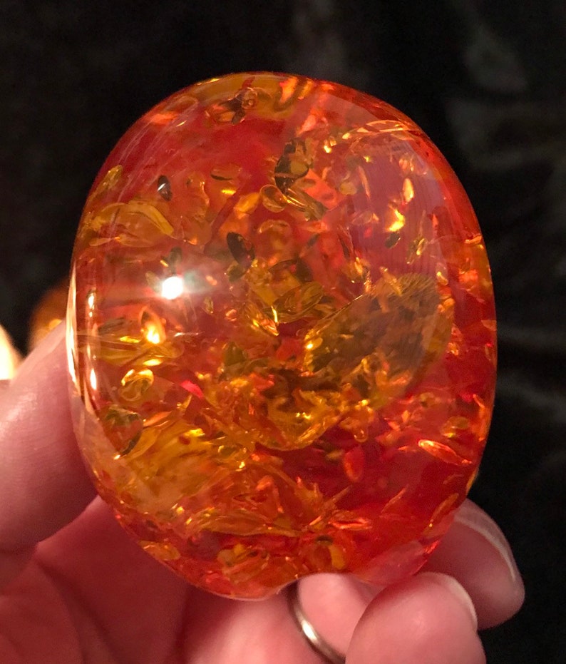 May include: A large, oval-shaped piece of amber with a reddish-orange hue and intricate patterns of golden inclusions.