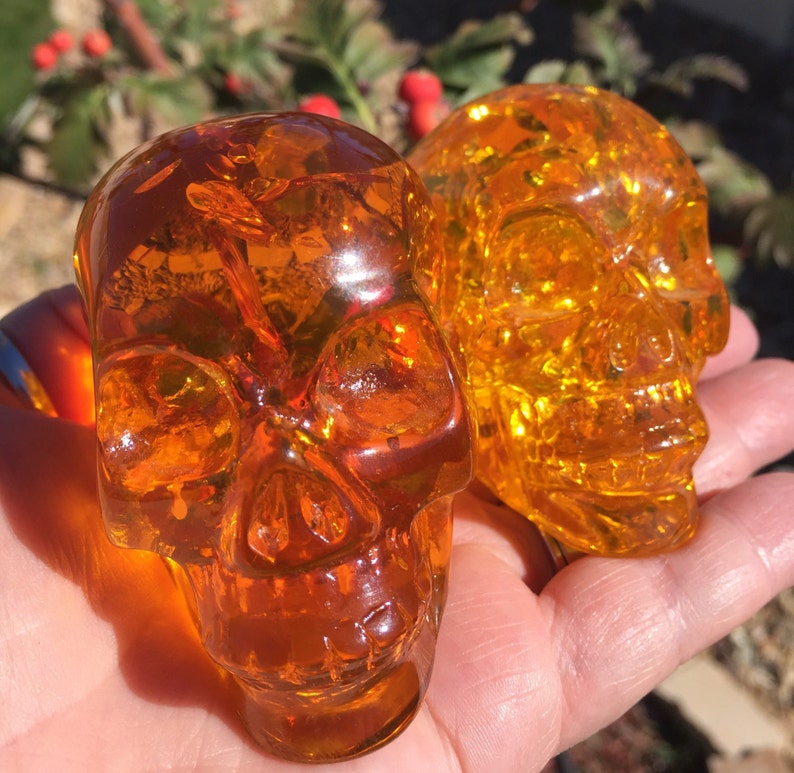 May include: Two amber glass skull figurines. The skulls are detailed and have a translucent, almost honey-like appearance.