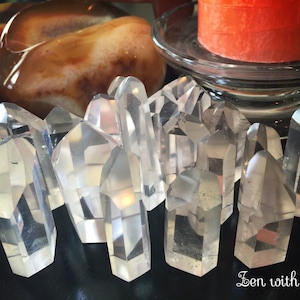 May include: A group of clear quartz crystal points arranged on a black surface. The crystals are various sizes and shapes, with some having a slight smoky tint. The crystals are arranged in a random pattern, with some overlapping each other. The image is taken from a close-up perspective, and the crystals are in focus. The background is out of focus, and the image has a soft, natural light.