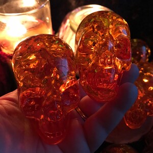 May include: A set of four amber glass skull ornaments with a glittery finish. The skulls are translucent and have a detailed design.