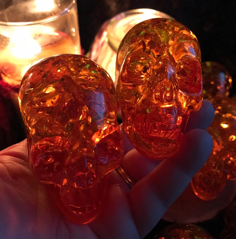 May include: A set of four amber glass skull ornaments with a glittery finish. The skulls are translucent and have a detailed design.