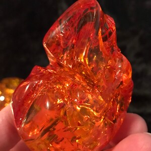 May include: A large, orange, translucent, irregularly shaped, glass paperweight. The paperweight has a swirling, marbled pattern.