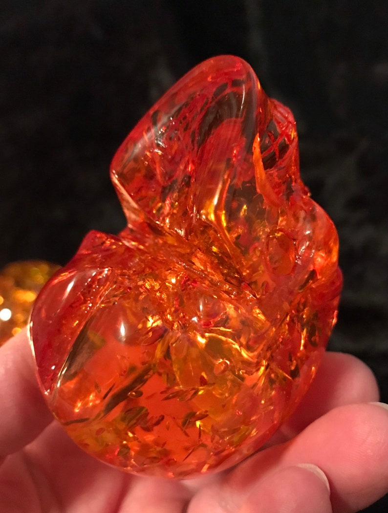 May include: A large, orange, translucent, irregularly shaped, glass paperweight. The paperweight has a swirling, marbled pattern.
