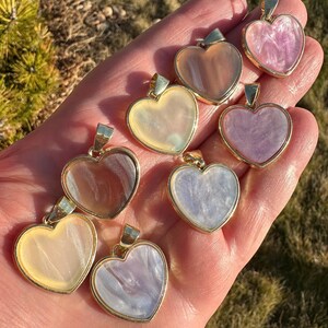 May include: Seven heart-shaped pendants with gold trim. The pendants are made of iridescent mother-of-pearl in various shades of pink, white, and brown.
