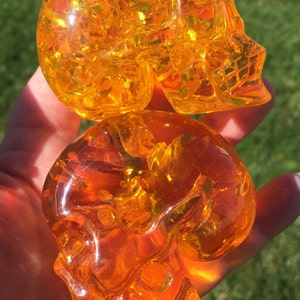 May include: Two orange glass skull sculptures. The skulls are translucent and have a detailed design.
