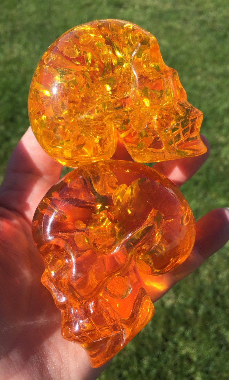 May include: Two orange glass skull sculptures. The skulls are translucent and have a detailed design.