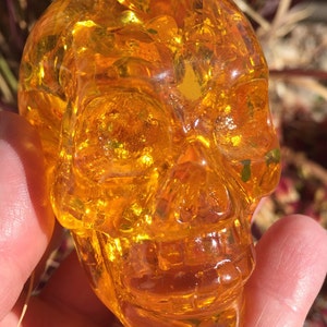 May include: A small, amber-coloured glass skull. The skull is detailed and has a smooth, polished finish.