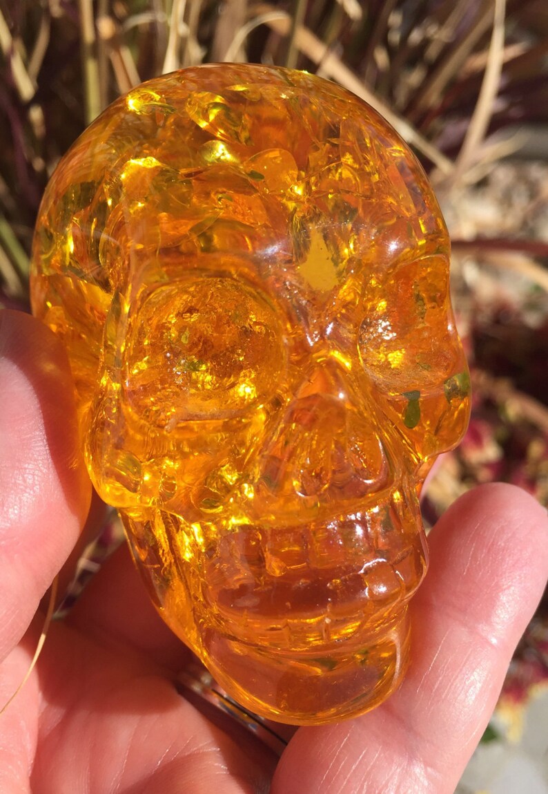 May include: A small, amber-coloured glass skull. The skull is detailed and has a smooth, polished finish.