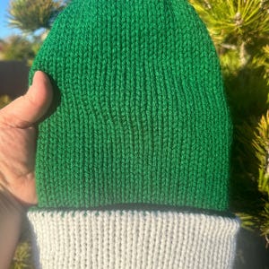May include: A green knitted beanie with a white brim. The beanie is made of a soft, textured yarn.