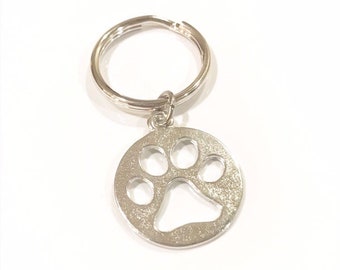 May include: Silver key chain with a paw print charm. The charm is a circle with a cut-out paw print design.