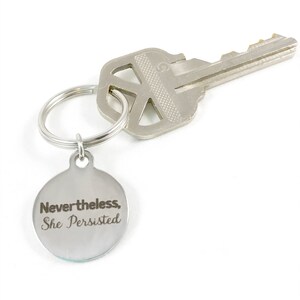 Flatlay of silver keyring with quote, "Nevertheless, she persisted."