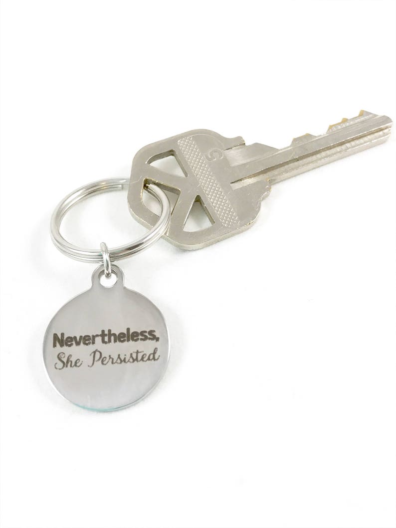 Flatlay of silver keyring with quote, "Nevertheless, she persisted."