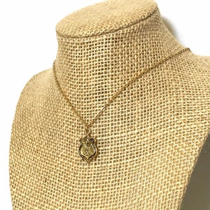 A gold tone brass pendant with fleur de lis design dangles from a 16k gold plated chain with lobster clasp closure. Necklace is displayed on a burlap neck form.