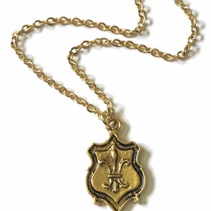 Close-up of gold tone brass pendant with fleur de lis design and 16k gold plated chain.