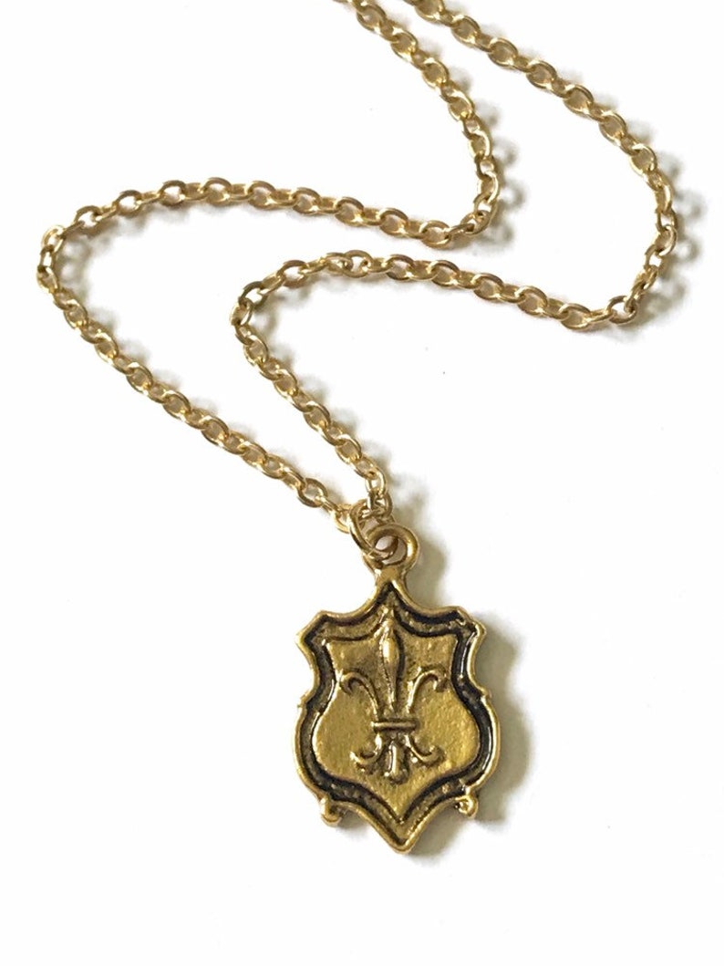Close-up of gold tone brass pendant with fleur de lis design and 16k gold plated chain.