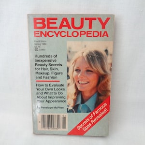 May include: Vintage "Beauty Encyclopedia" book from 1980. The cover features a smiling woman and the title in red letters. The book promises beauty secrets for hair, skin, makeup, figure, and fashion. The cover also includes the text "Secrets of Famous Spas Revealed!"