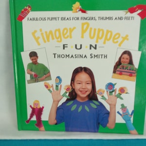 May include: A green book with the title "Finger Puppet Fun - Thomasina Smith" on the cover. The book features illustrations of finger puppets, including flowers, a bus, and a person. The book is about making finger puppets.