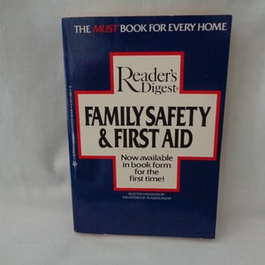 Peut inclure: Un livre bleu avec une croix rouge sur la couverture. Le titre est "Reader's Digest Family Safety & First Aid". Le livre est maintenant disponible en format livre pour la première fois.