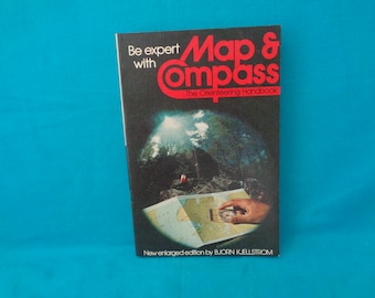 May include: A vintage book titled "Map & Compass: The Orienteering Handbook." The cover is black with red and white text, featuring a map and compass illustration. The book's title is in a bold, stylized font. The cover also includes the text "Be expert with" and "New enlarged edition by BJORN KJELLSTROM."