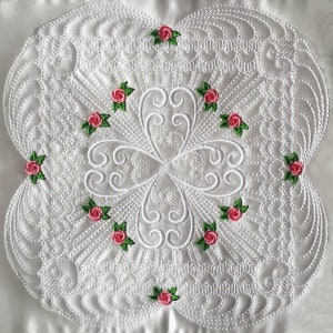 May include: White fabric with a detailed, intricate, embroidered design featuring a repeating pattern of swirls and small pink roses with green leaves.