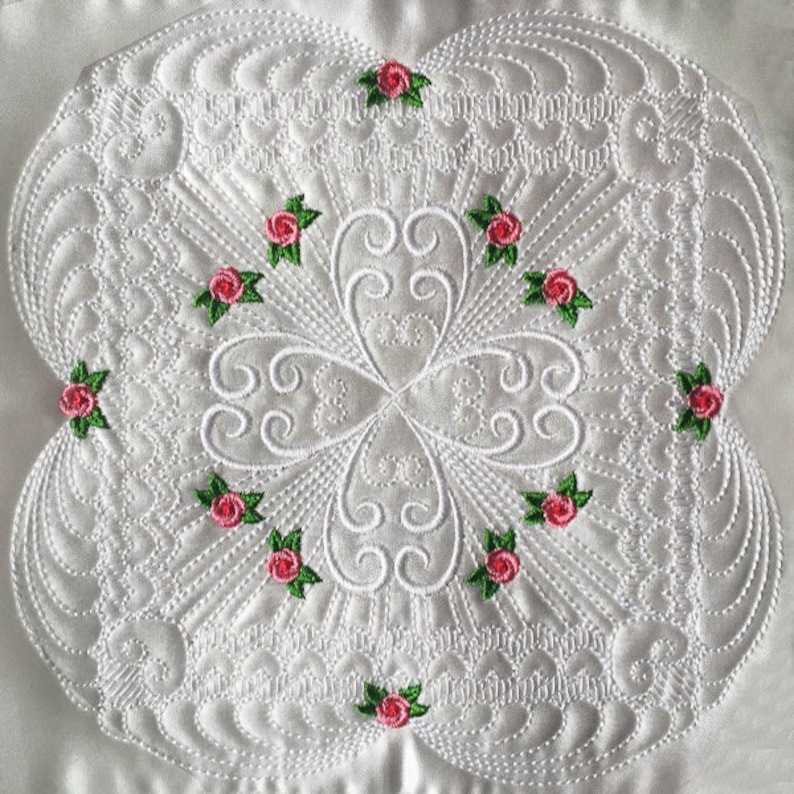 May include: White fabric with a detailed, intricate, embroidered design featuring a repeating pattern of swirls and small pink roses with green leaves.