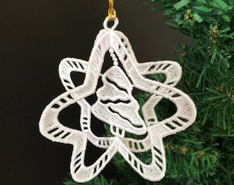 Può includere: Addobbo natalizio in pizzo bianco a forma di stella con una stella più piccola all'interno. L'addobbo è appeso a un filo dorato su un albero di Natale verde.