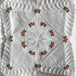 May include: White quilted fabric with a diamond pattern and a central starburst design. The fabric is decorated with small pink roses with green leaves.