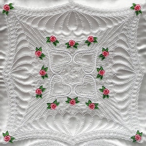 May include: White quilted fabric with a delicate pattern of hearts and swirls. The fabric is decorated with pink roses with green leaves.